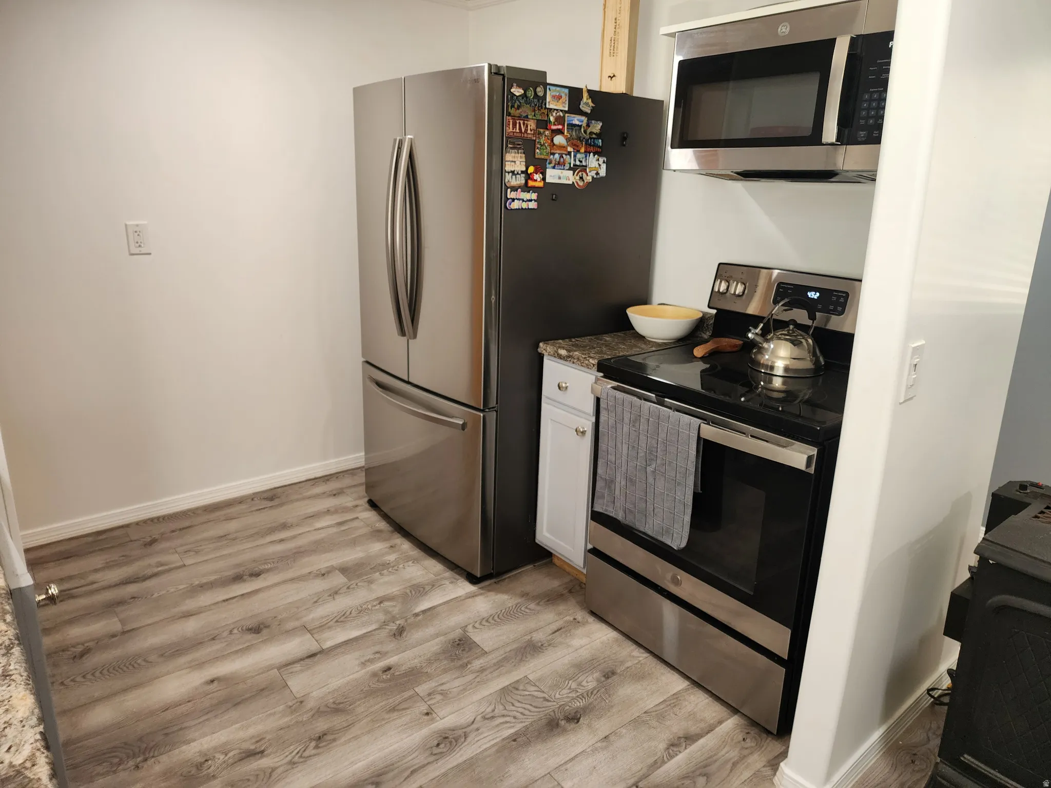 Stainless steel refrigerator, stainless steel over-the-range microwave, stainless steel range, white cabinetry, and wood-finish flooring