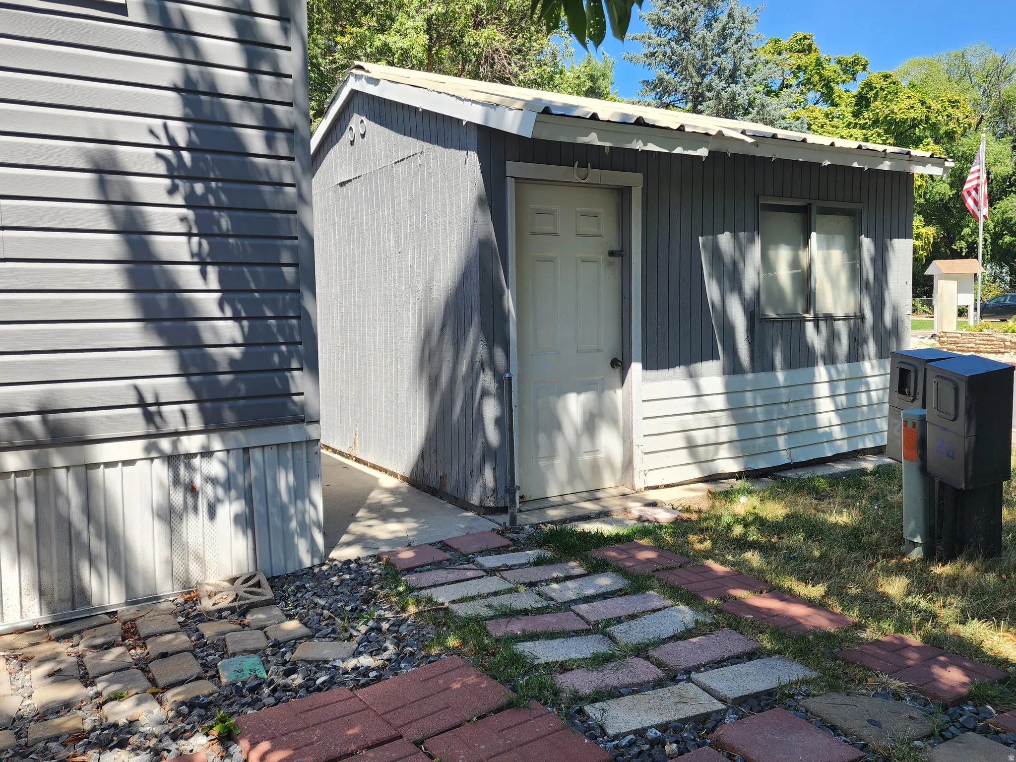 Storage shed with a white door, two windows, and corrugated metal roofing
