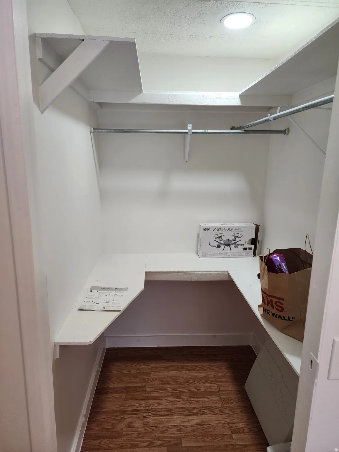 White-painted closet featuring built-in shelving, a metal hanging rod, and wood-finish flooring