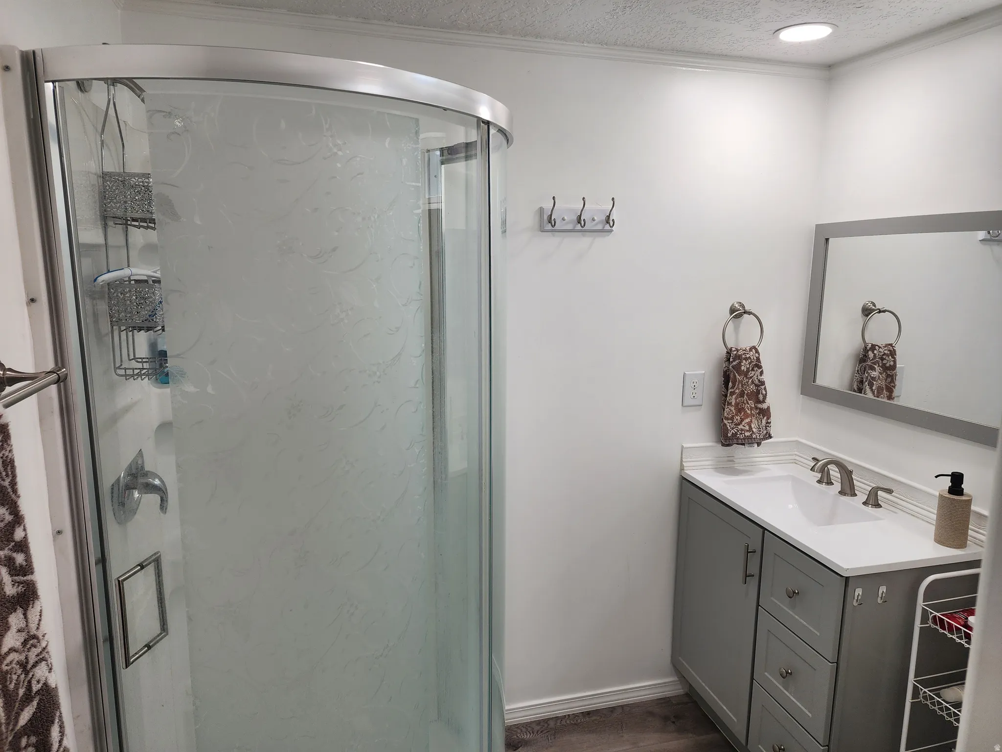 Curved glass shower enclosure with frosted detailing, vanity with integrated sink and storage, stone-finish countertop, brushed nickel faucet, and recessed ceiling lighting