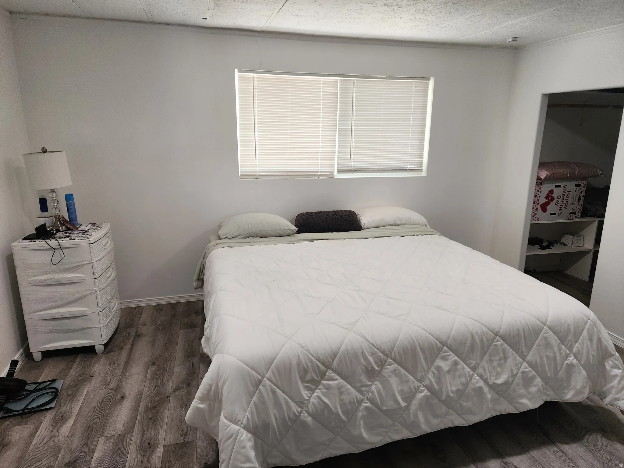 Wood-finish flooring throughout, bright white walls, and a window with blinds providing natural illumination