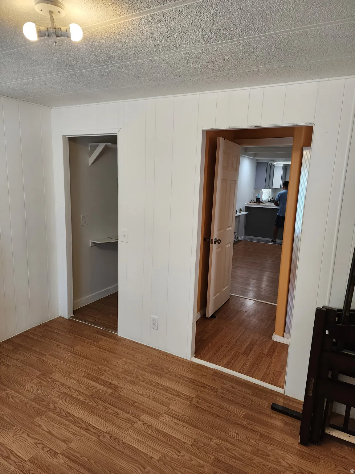 Wood-finish flooring throughout, white paneled walls, and a textured ceiling