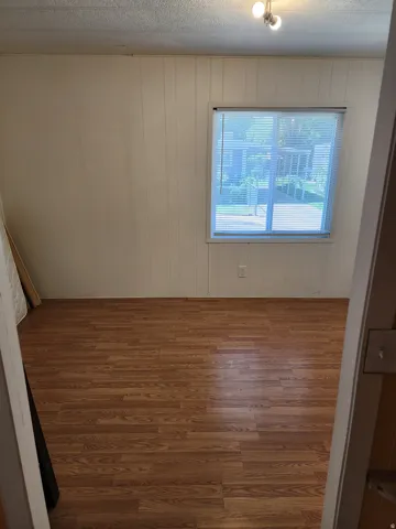 Room featuring wood-finish flooring, vertical paneling on walls, a window with blinds, and ceiling-mounted lighting