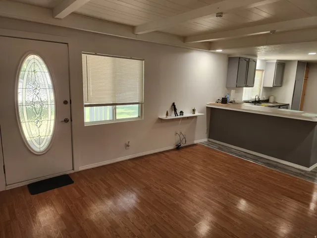 Wood-finish flooring, exposed beam ceiling, decorative oval glass insert door, recessed lighting, and kitchen pass-through counter with gray cabinetry