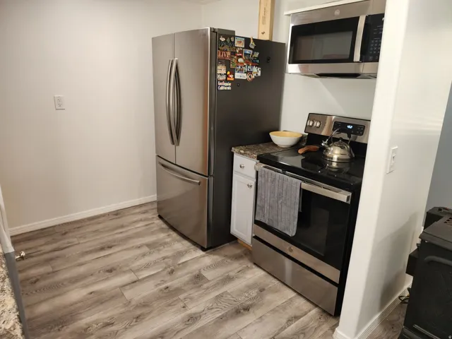 Stainless steel refrigerator, stainless steel over-the-range microwave, stainless steel range, white cabinetry, and wood-finish flooring