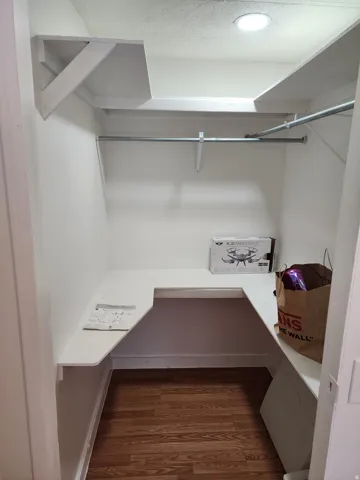 White-painted closet featuring built-in shelving, a metal hanging rod, and wood-finish flooring