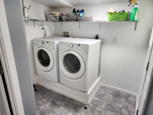 Dedicated laundry area with durable flooring, built-in shelving, and white appliances