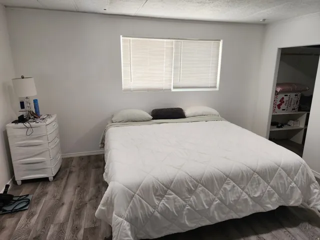 Wood-finish flooring throughout, bright white walls, and a window with blinds providing natural illumination