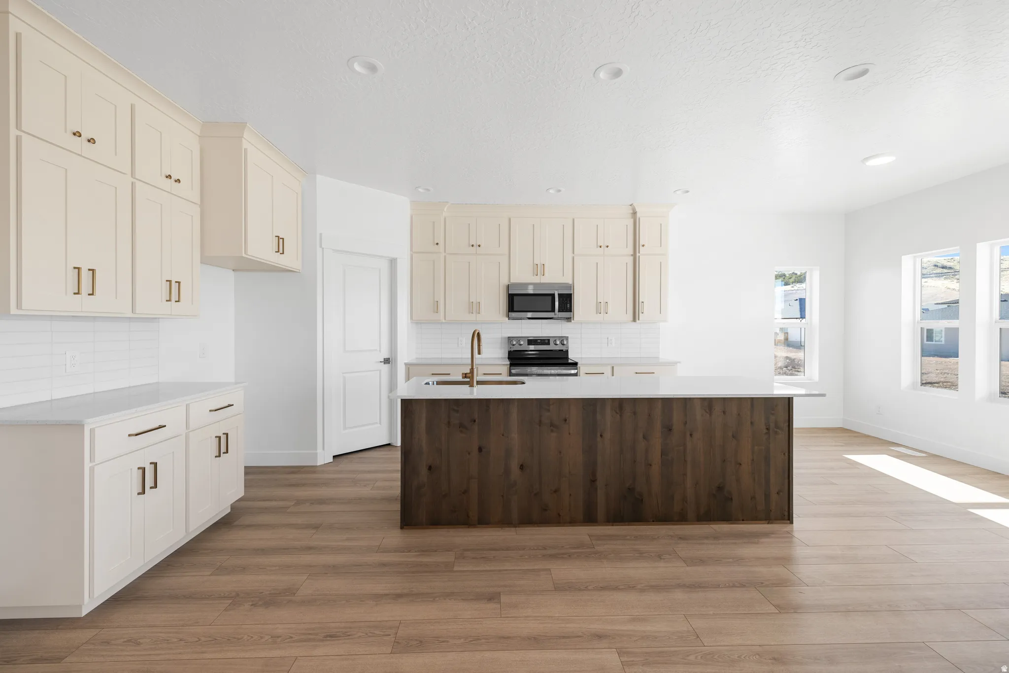 Kitchen featuring light-toned cabinetry, a wood-finish island with a light countertop, stainless steel appliances, a white tile backsplash, and recessed lighting