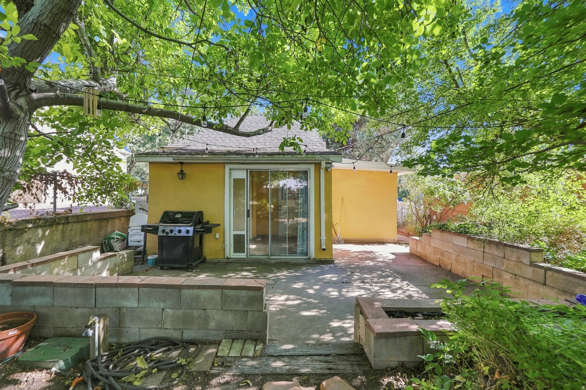 Poured concrete patio with block retaining walls, built-in fire pit, and mature shade trees