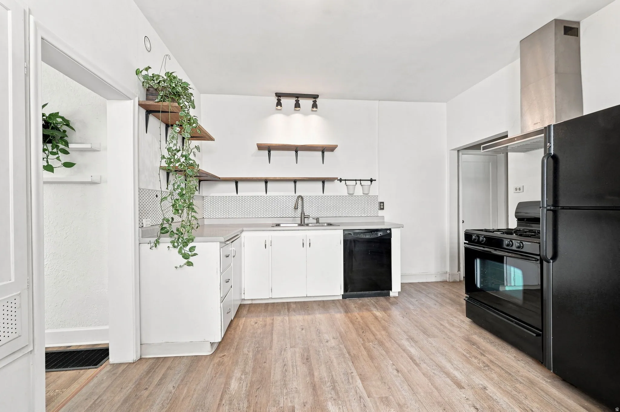 Kitchen featuring wood-finish flooring, white cabinetry, integrated sink, black dishwasher, and black refrigerator