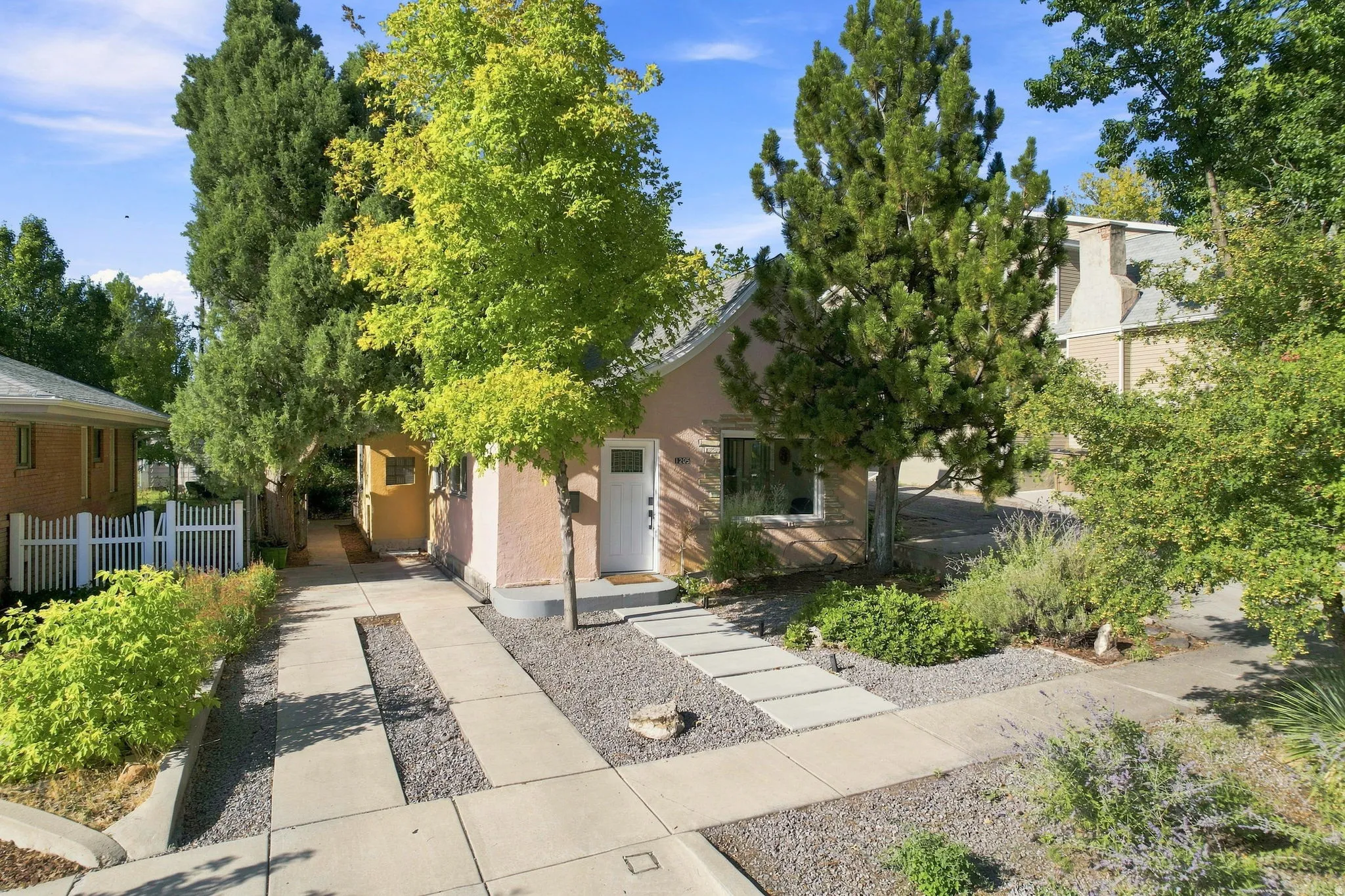 Stucco exterior with a white entry door, front walkway with stepping stones, gravel landscaping, and mature trees