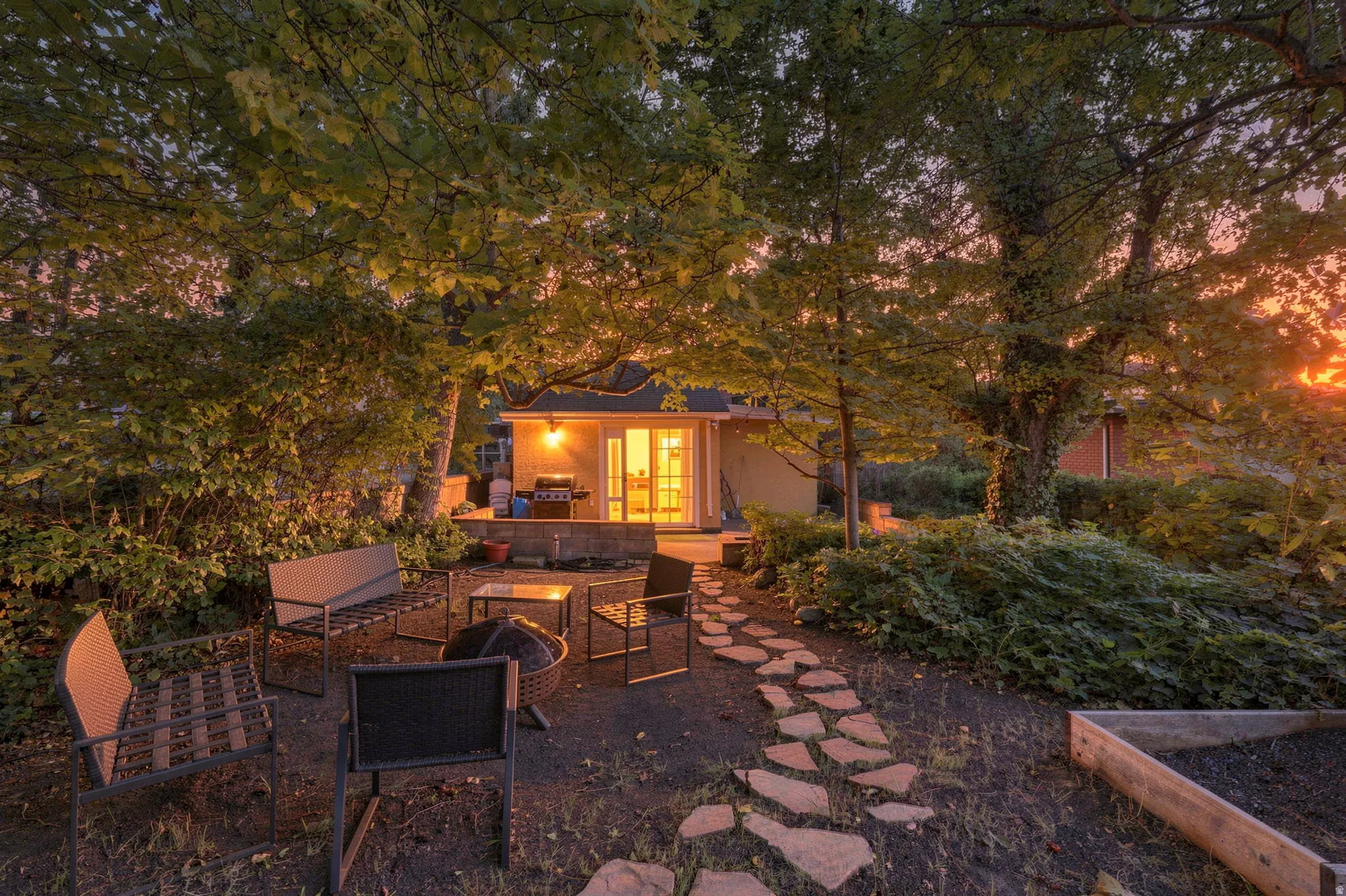 Landscaped yard with mature trees, stone pathway, and a patio with an exterior structure featuring French doors