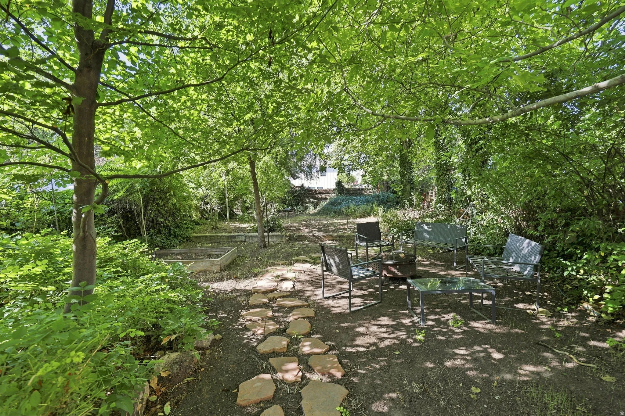 Shaded outdoor area featuring mature trees, a stepping stone pathway, and built-in garden beds