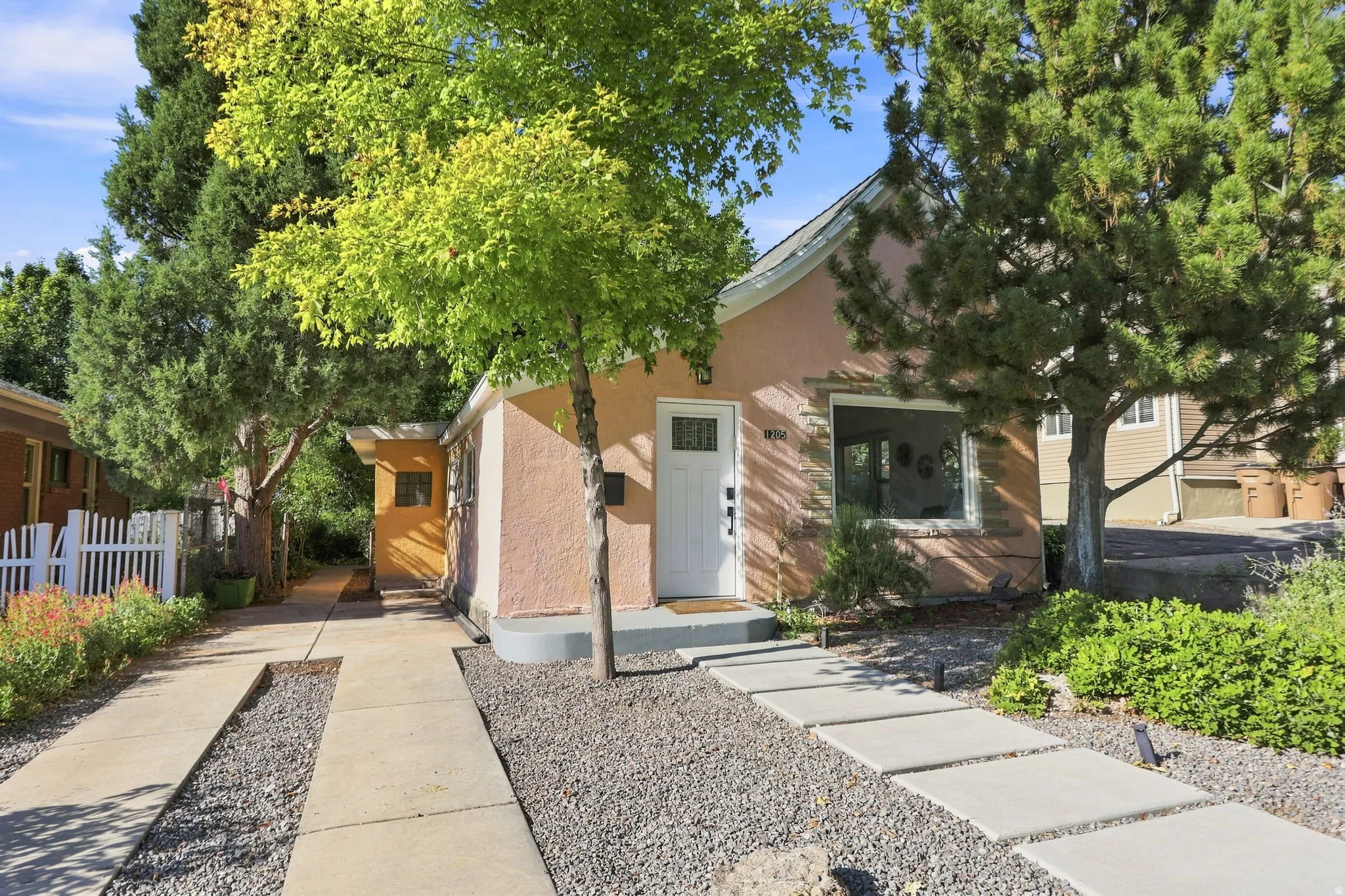 Stucco exterior with a white entry door, concrete stepping stones, gravel landscaping, and mature trees