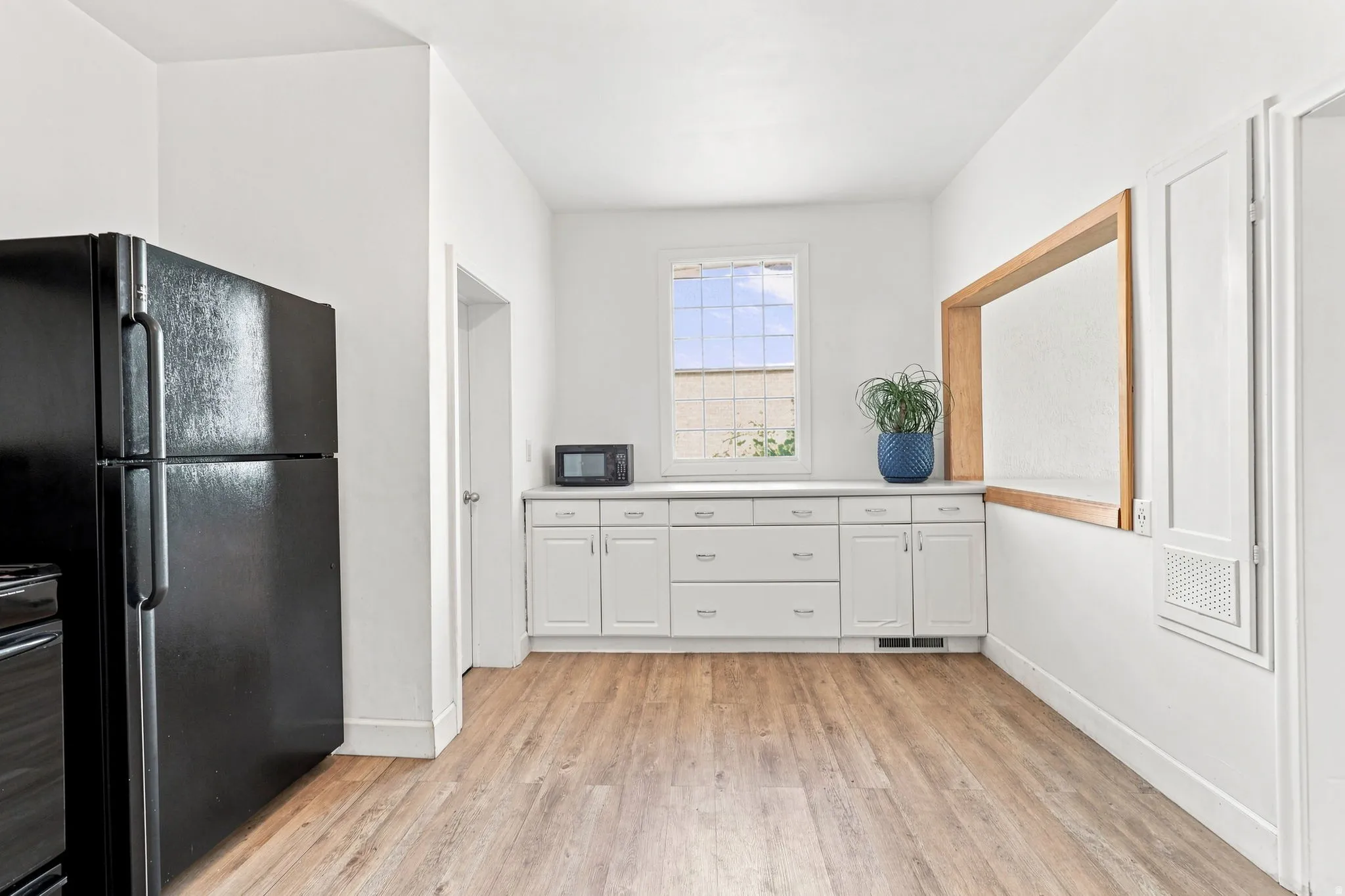 Wood-finish flooring, white cabinetry with silver hardware, white countertops, and a wood-framed pass-through window