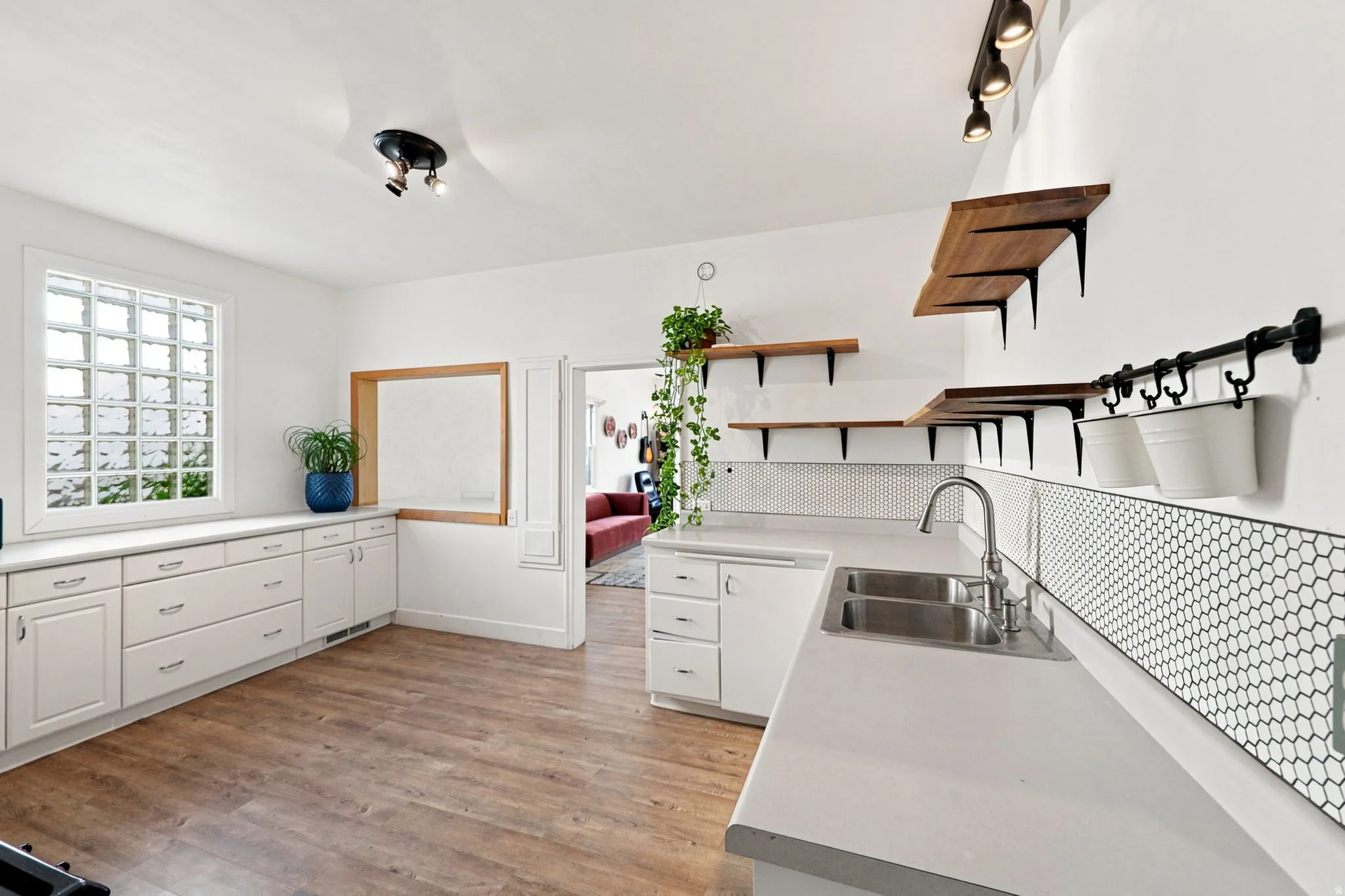 Contemporary kitchen featuring white cabinetry, light countertops, wood-finish flooring, and open wood shelving