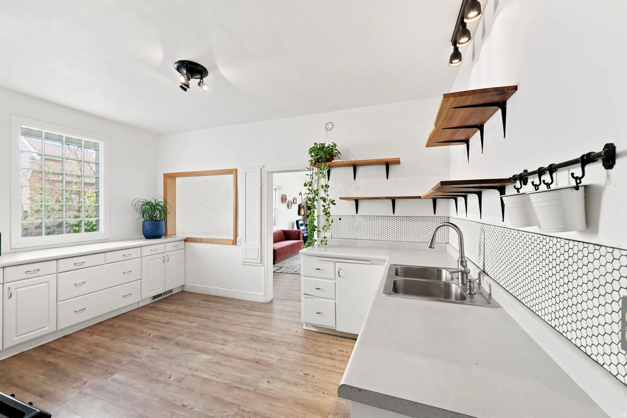 White cabinetry with brushed nickel hardware, light-toned wood-finish flooring, white countertops, and a double basin stainless steel sink