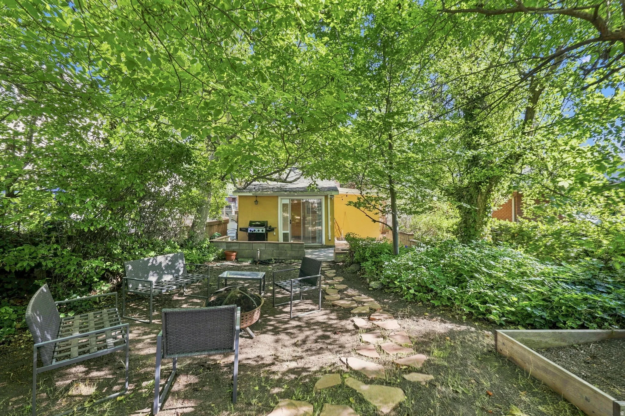 Private backyard with mature trees, a stone paver pathway, and an elevated patio area