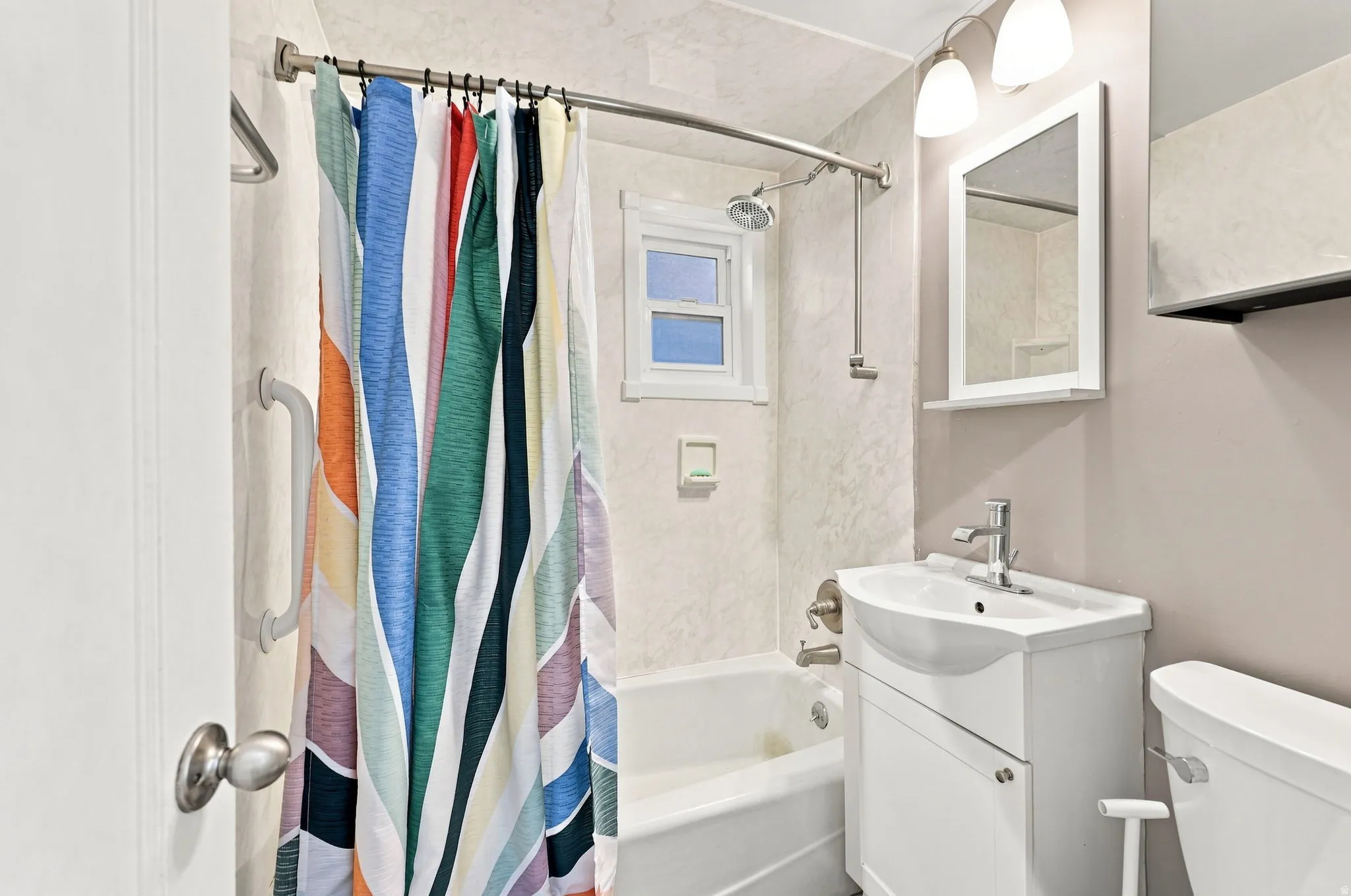 Bathtub with shower fixture, white vanity with integrated sink, wall-mounted mirror, and overhead lighting