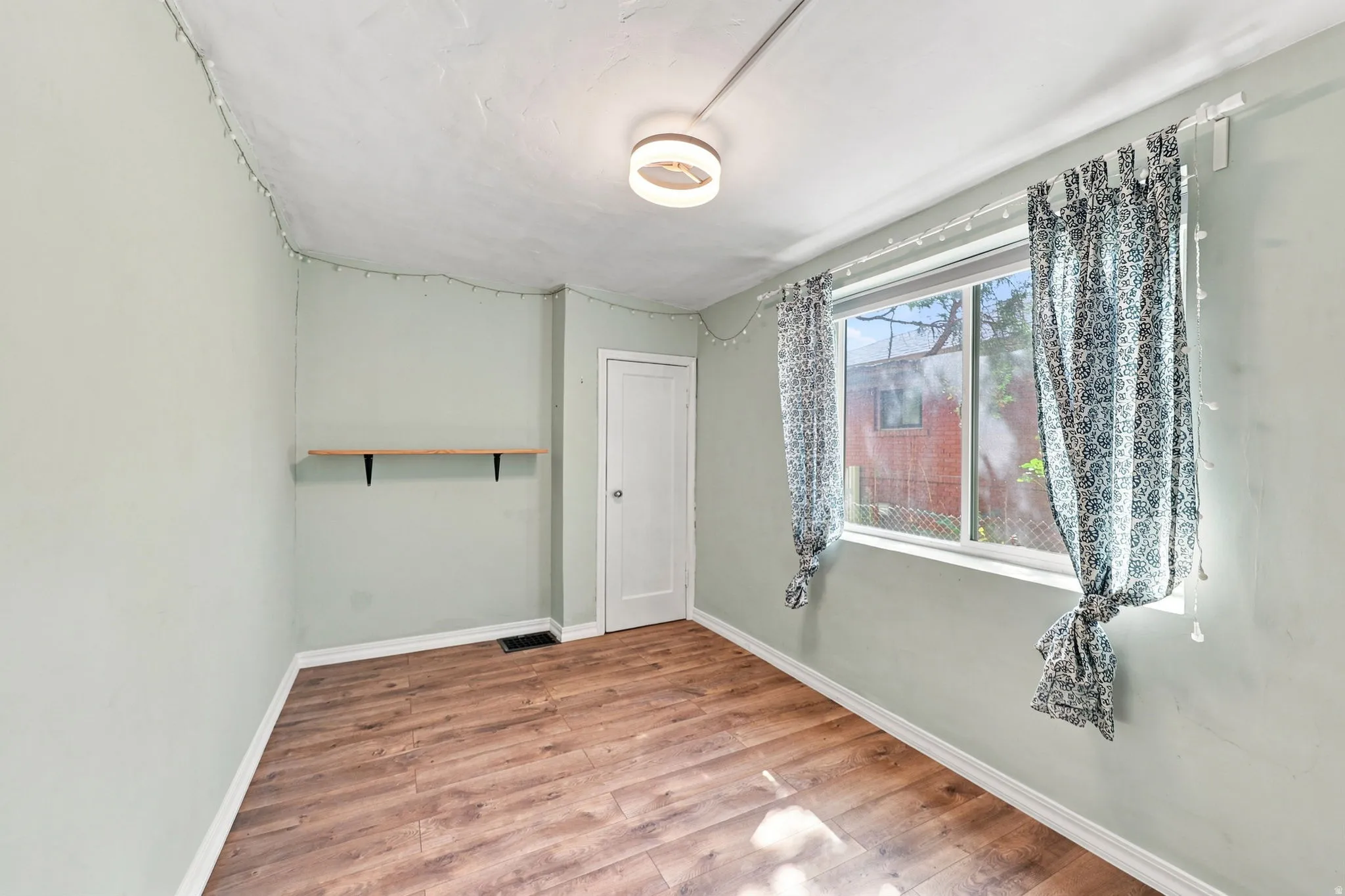 Wood-finish flooring, single-pane window, flush-mount ceiling light, built-in shelving, white door