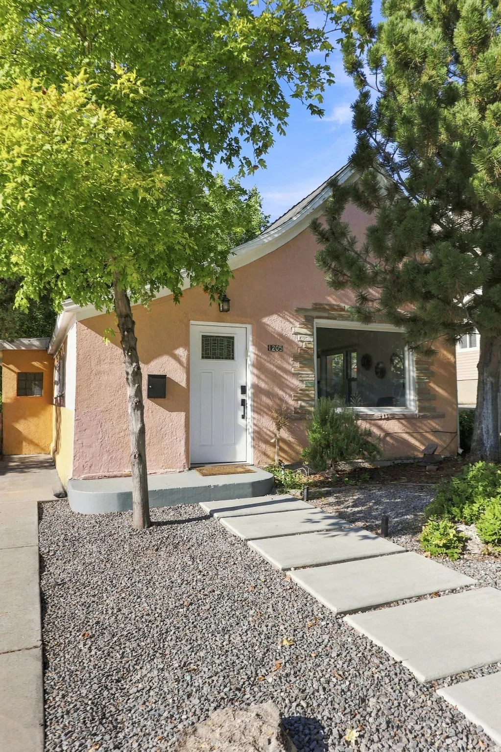 Stucco exterior with stone accent, white entry door, multiple windows, concrete step pathway, and gravel landscaping
