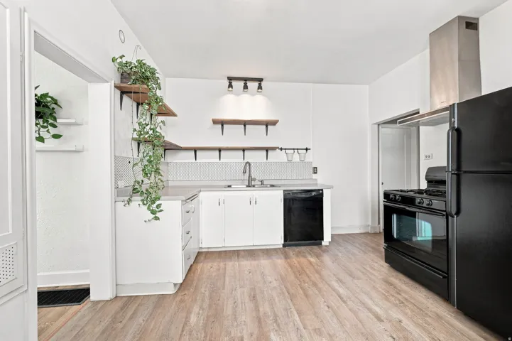 Kitchen featuring wood-finish flooring, white cabinetry, integrated sink, black dishwasher, and black refrigerator