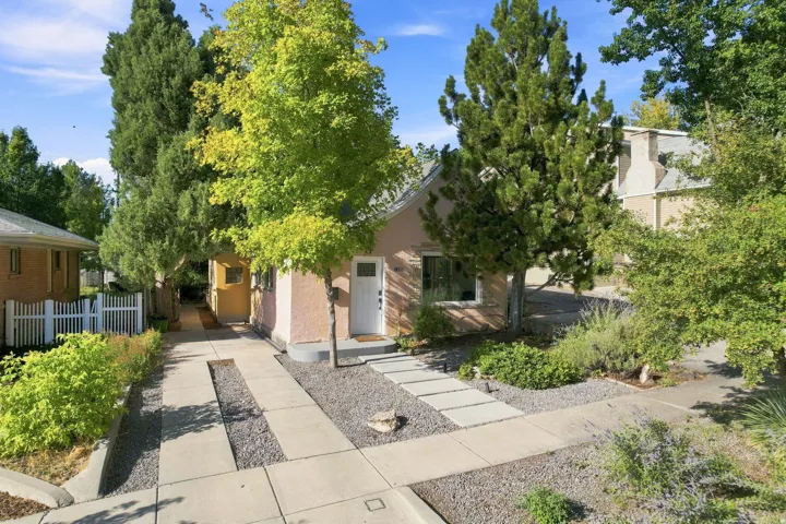 Stucco exterior with a white entry door, front walkway with stepping stones, gravel landscaping, and mature trees