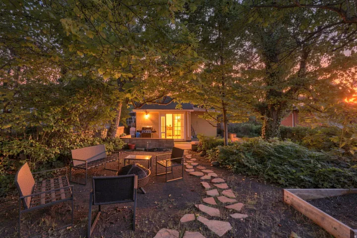Landscaped yard with mature trees, stone pathway, and a patio with an exterior structure featuring French doors