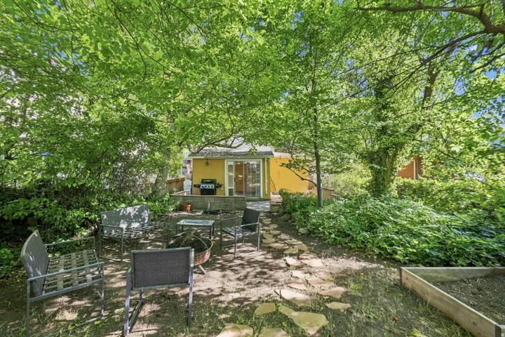 Private backyard with mature trees, a stone paver pathway, and an elevated patio area
