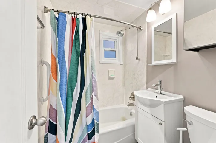 Bathtub with shower fixture, white vanity with integrated sink, wall-mounted mirror, and overhead lighting