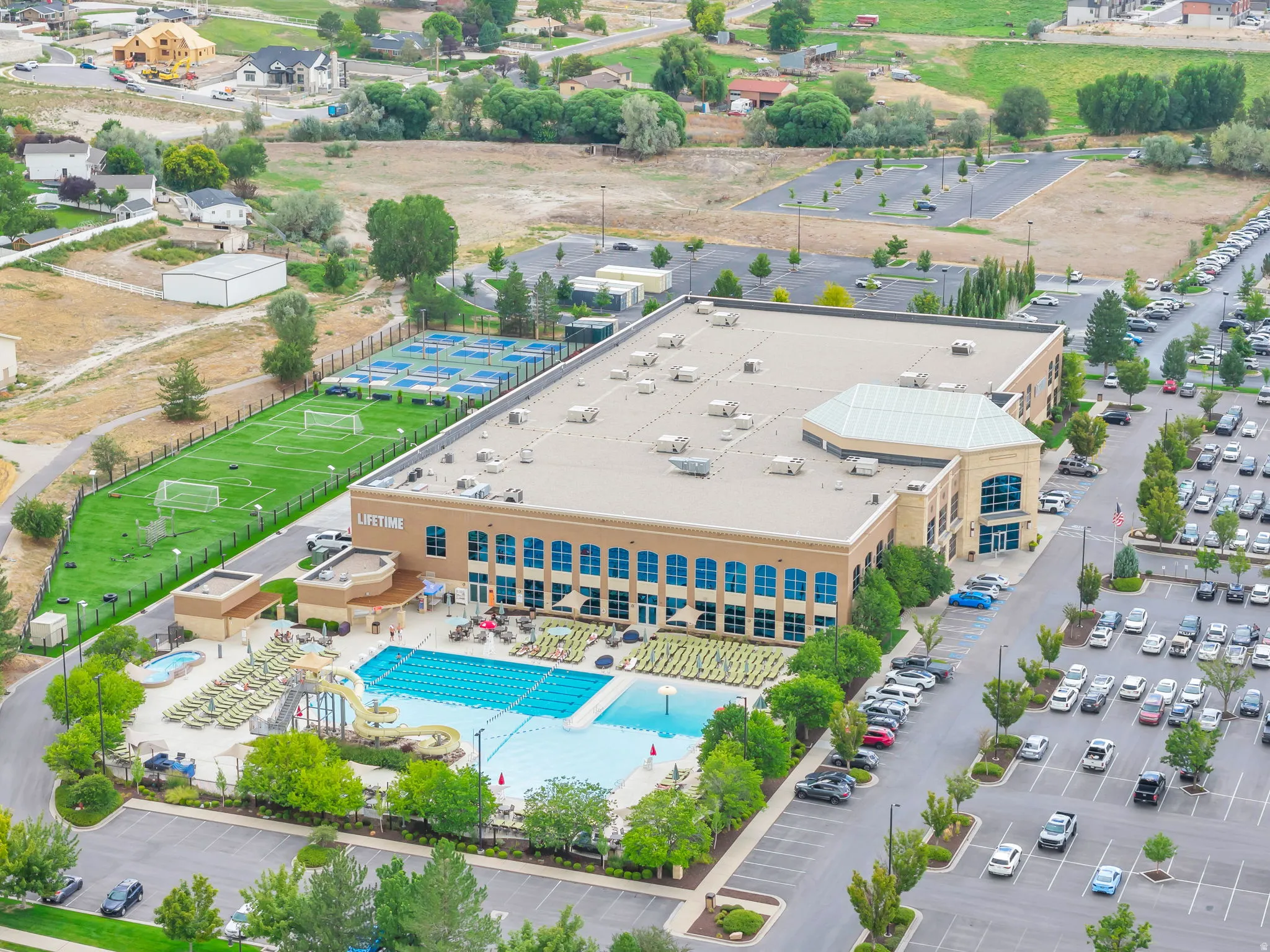 Large commercial building featuring an expansive outdoor pool area, multiple tennis courts, and a manicured soccer field