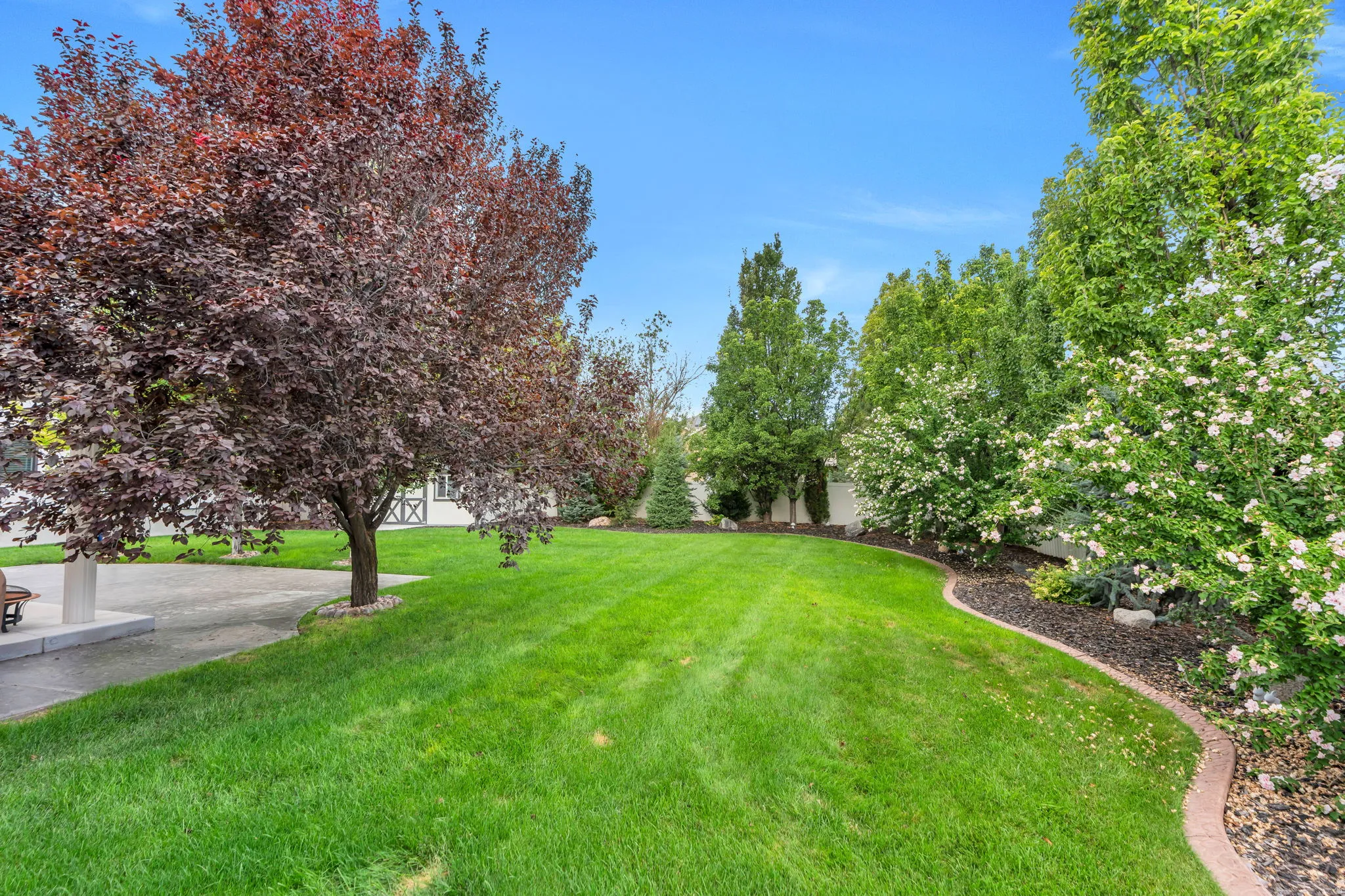 Expansive lawn with mature trees and a curved landscape bed featuring decorative rock
