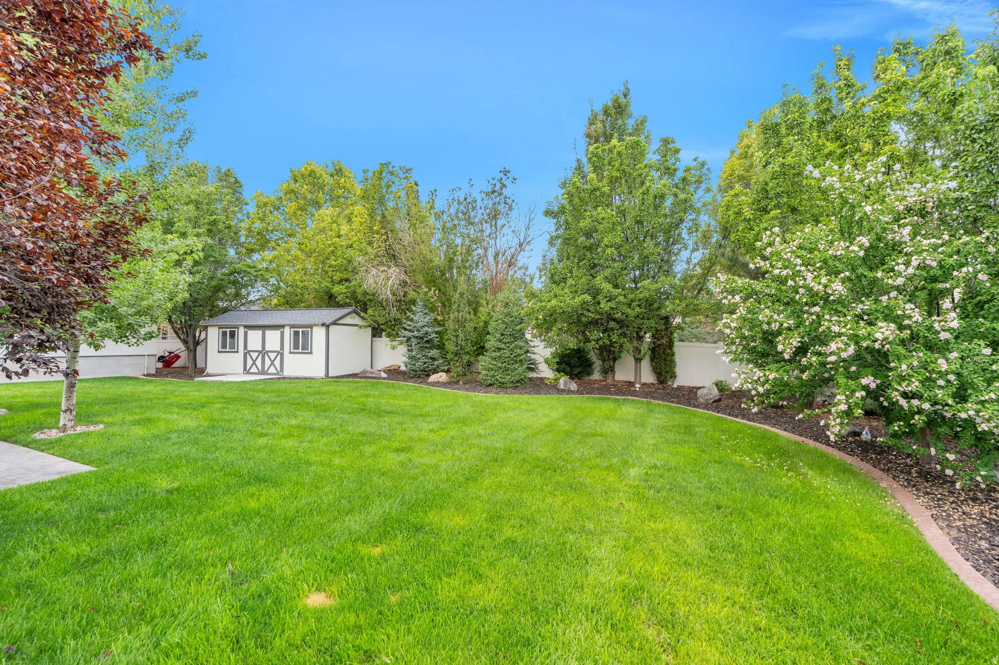Expansive lawn area, detached storage shed with double cross-buck doors, mature trees, and landscaped borders