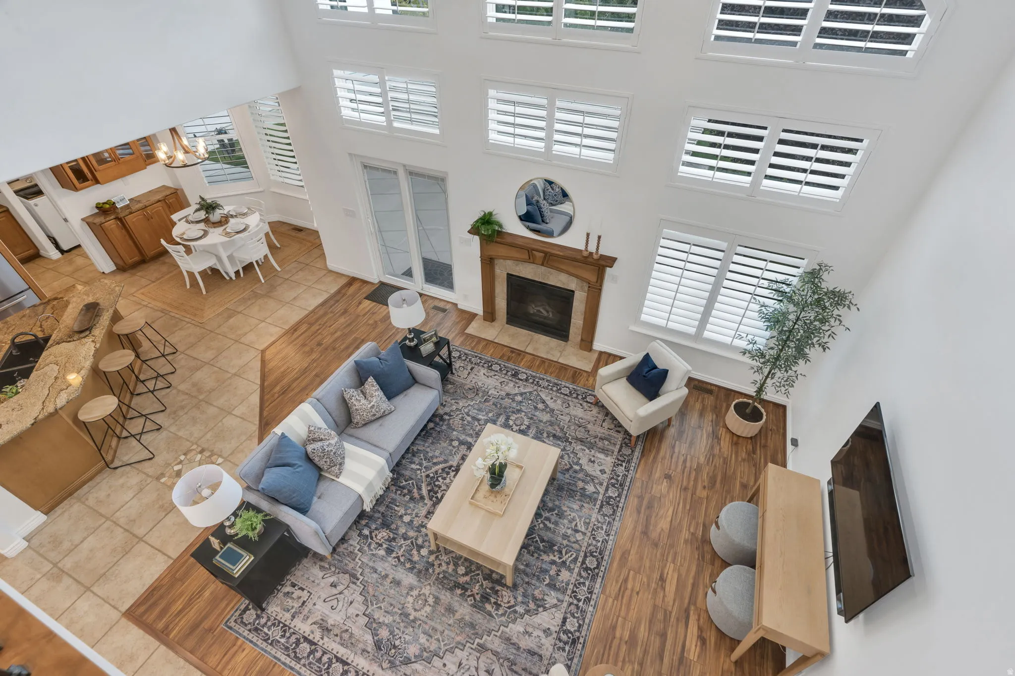 Two-story living area with high ceilings, multiple windows with plantation shutters, wood-finish flooring, and a fireplace with a wood mantle