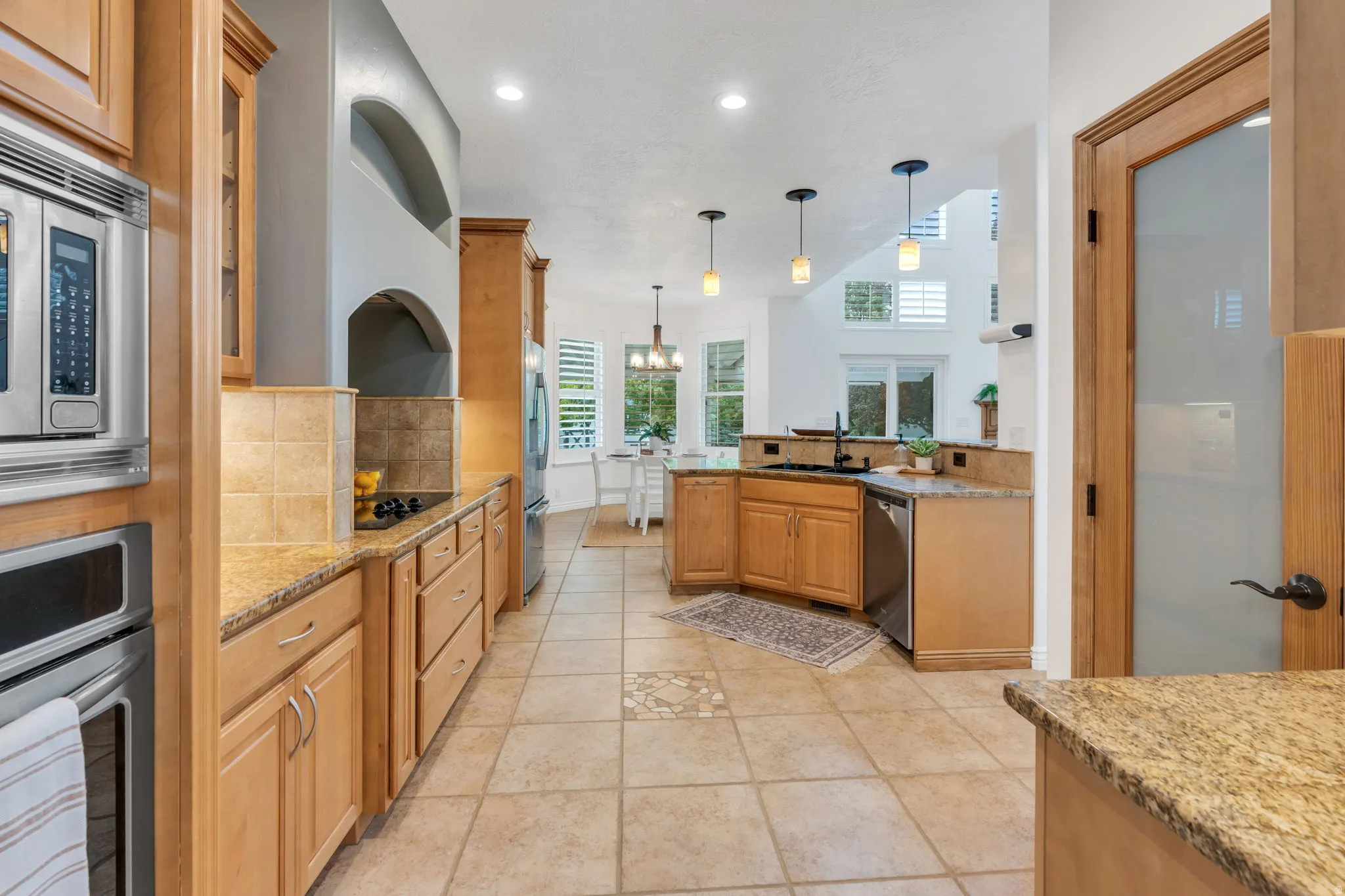 Kitchen featuring light wood cabinetry, stone countertops, stainless steel appliances, tile flooring, and pendant lighting