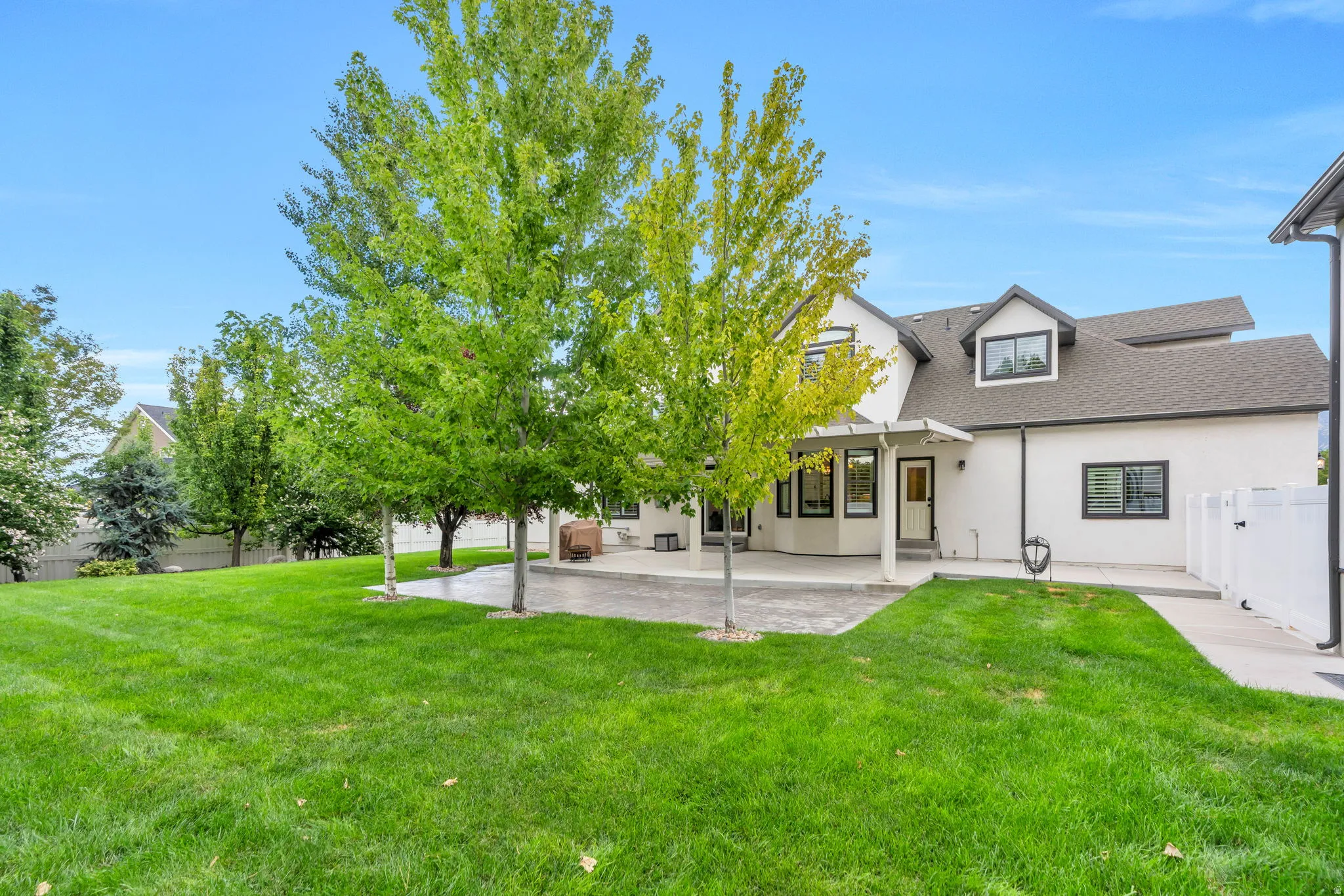 Expansive green lawn, mature trees, concrete patio, white stucco exterior, black-framed windows