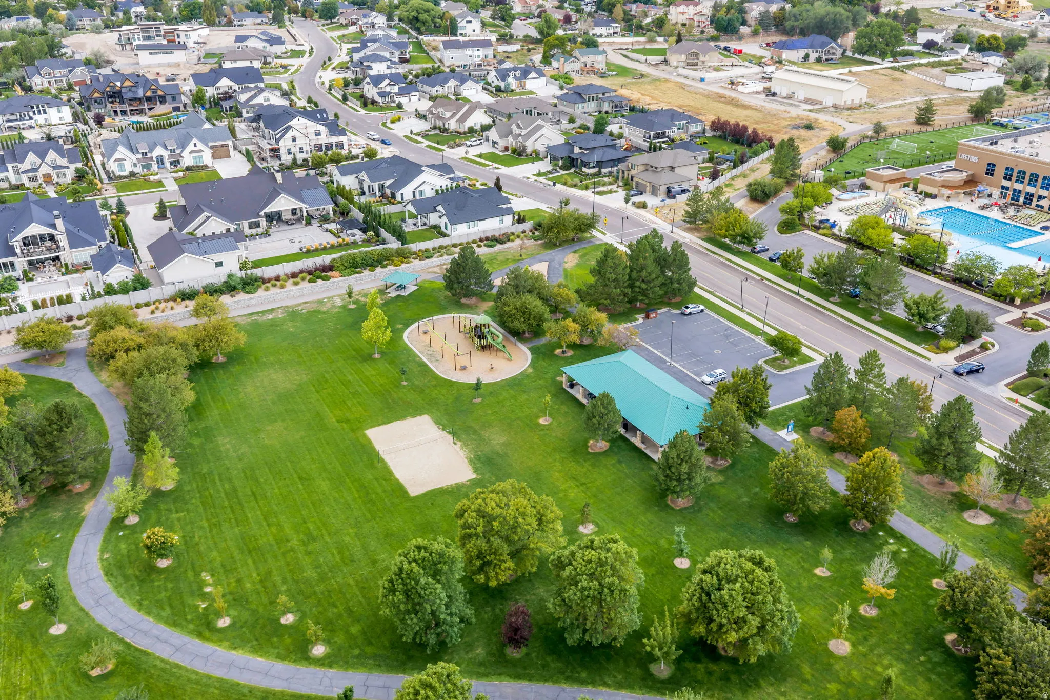 Expansive green space featuring walking paths, a children's play area, a covered pavilion, and sports courts