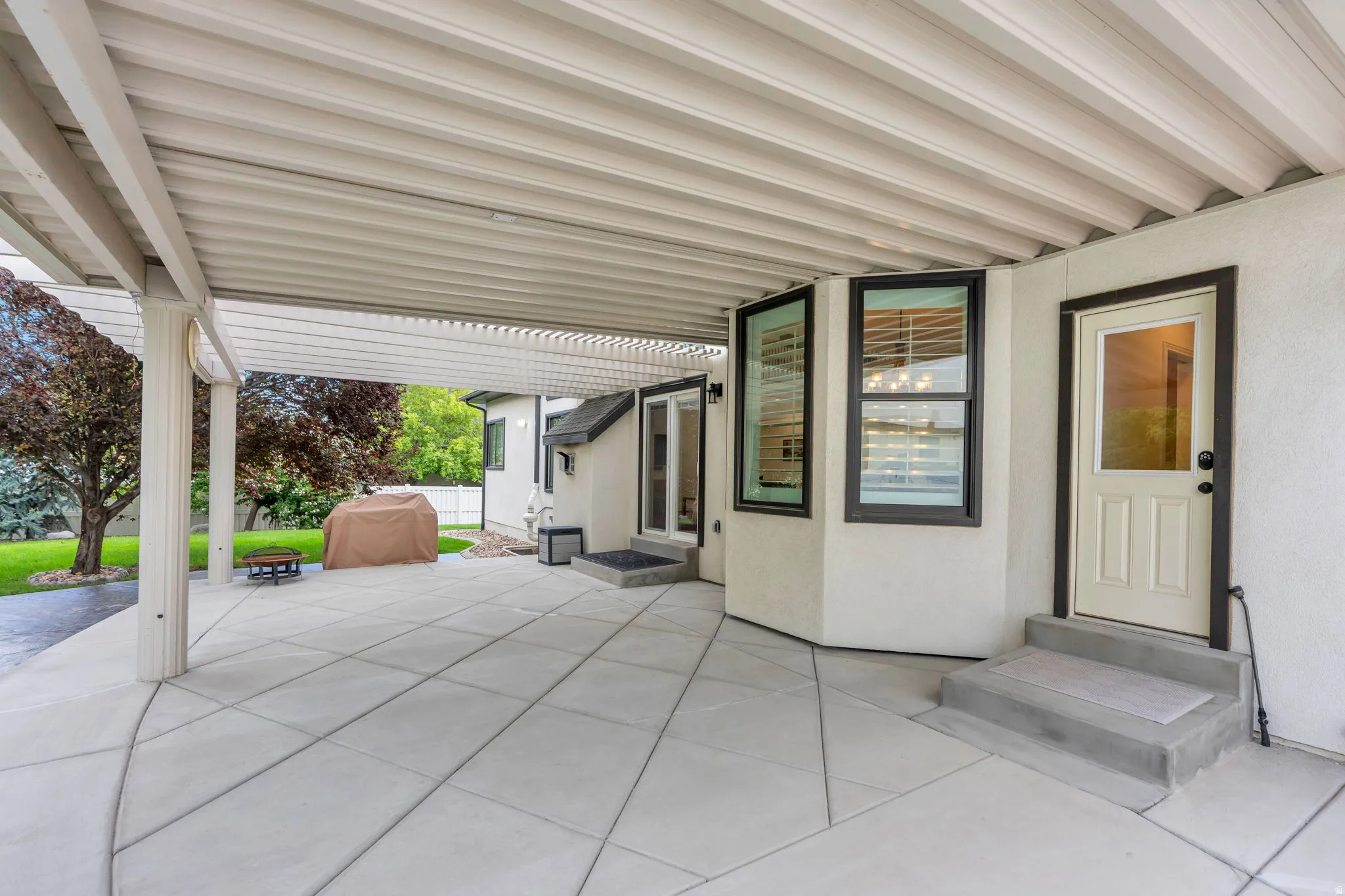 Expansive concrete patio with a covered pergola, stucco exterior, and multiple exterior doors