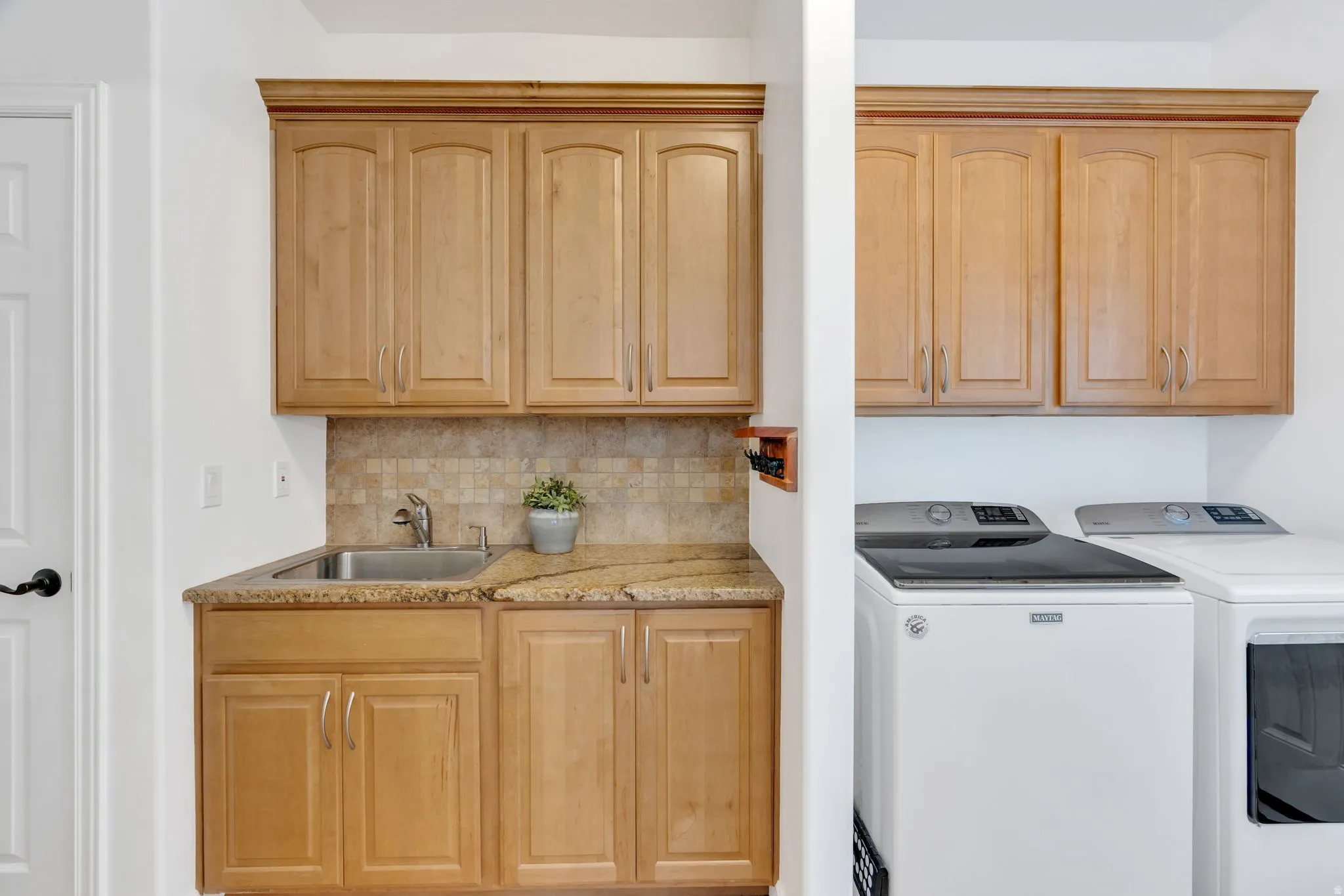 Wood-finish cabinetry, granite-style countertop, stainless steel sink, and tile backsplash