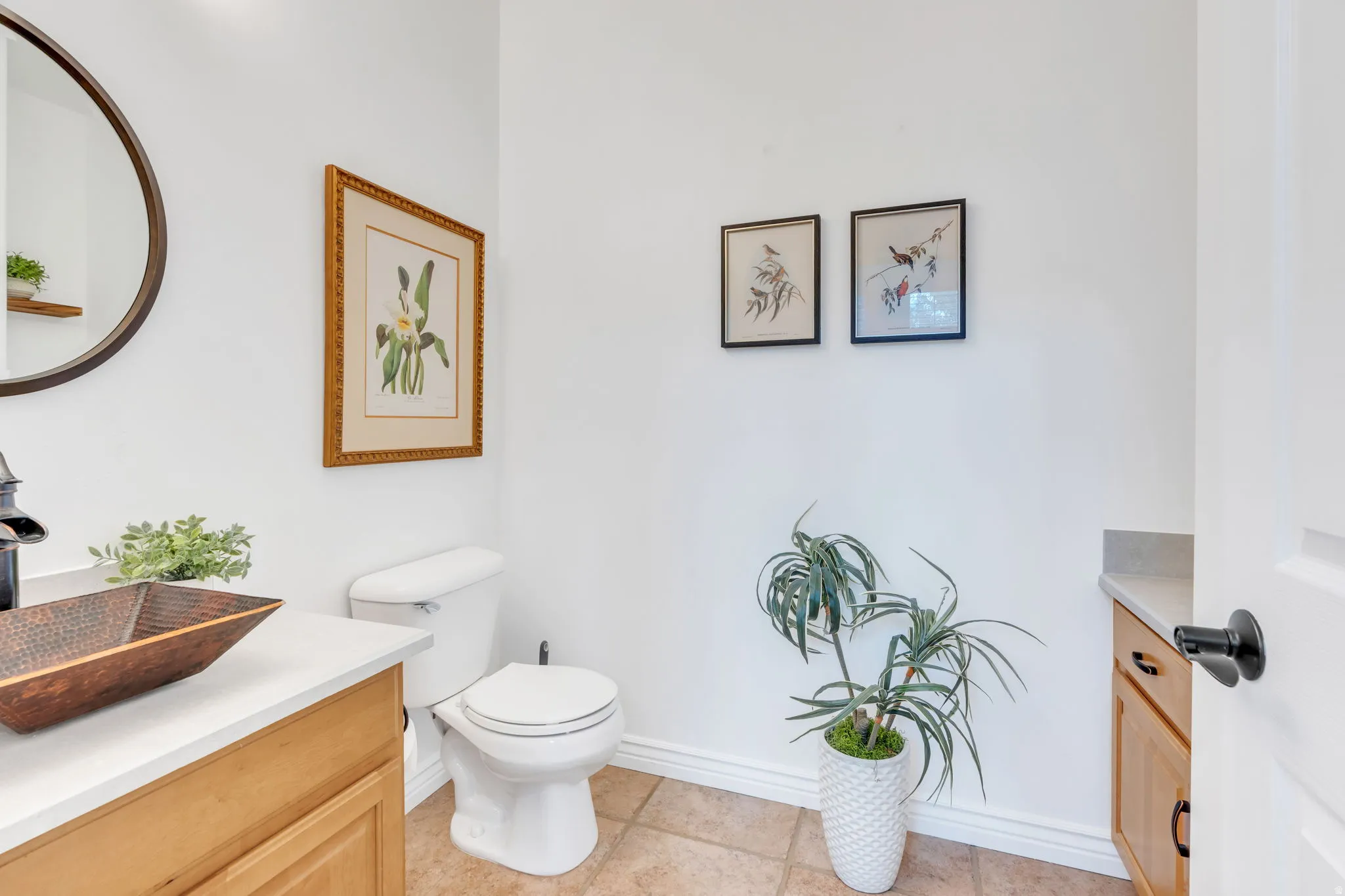 Single-handle oil-rubbed bronze faucet with a bronze vessel sink, light wood-finish vanity, and a round wall mirror