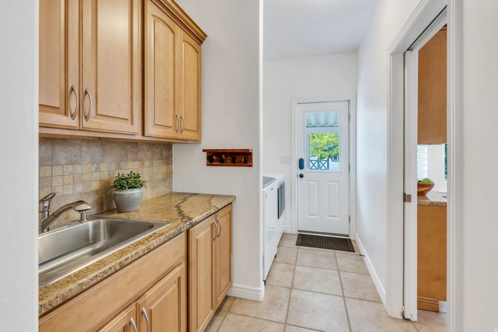 Light wood-finish cabinetry, stainless steel sink, tiled backsplash, granite-finish countertop, and tile flooring