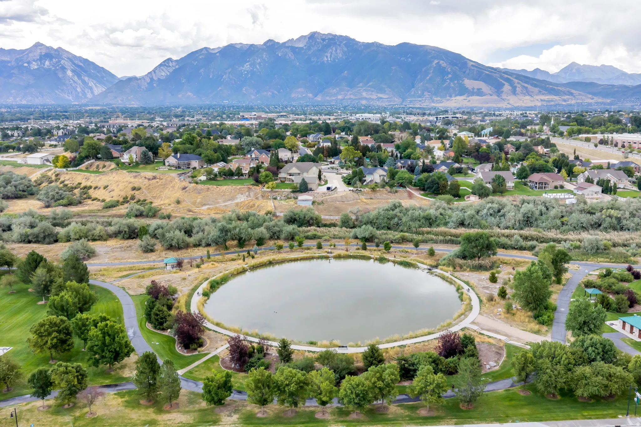 Aerial perspective showcasing a circular pond surrounded by paved pathways and mature trees