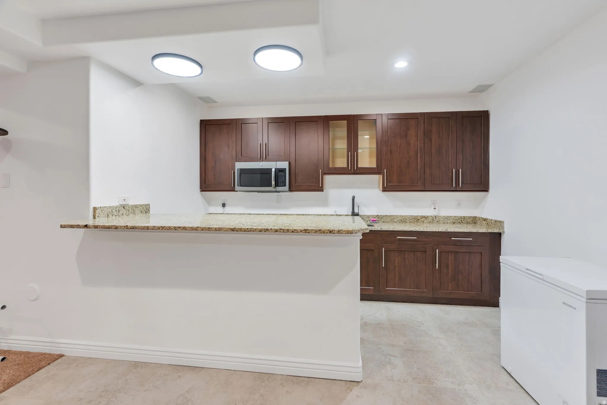 Built-in cabinetry with glass-front accents, stainless steel microwave, and stone countertops