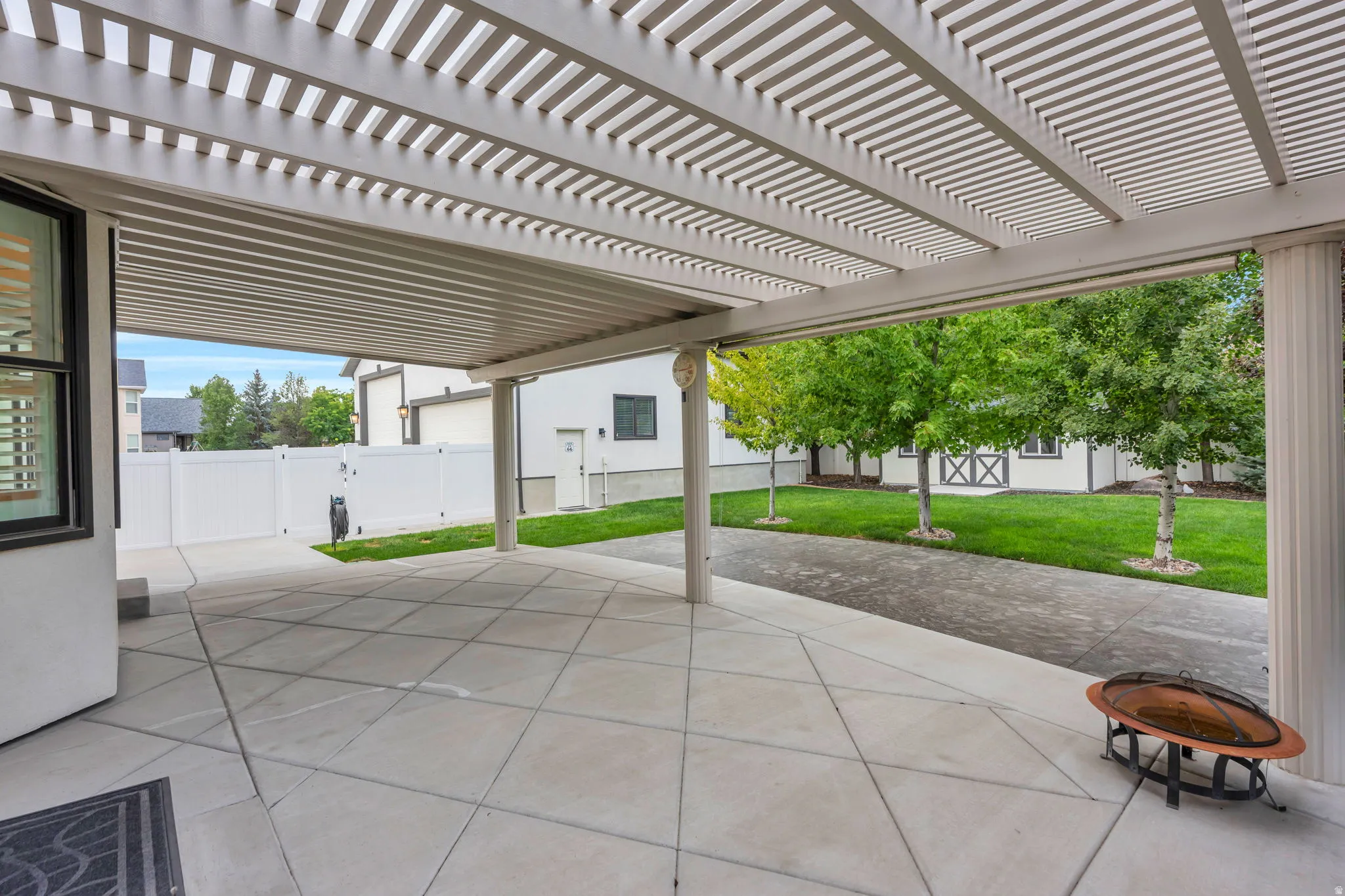 Covered patio area featuring a slatted pergola roof and concrete paver flooring