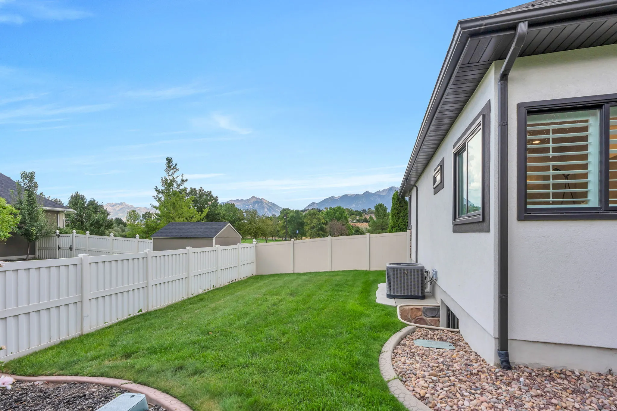 Stucco exterior with dark trim, featuring a manicured lawn, a white privacy fence, and a gravel perimeter