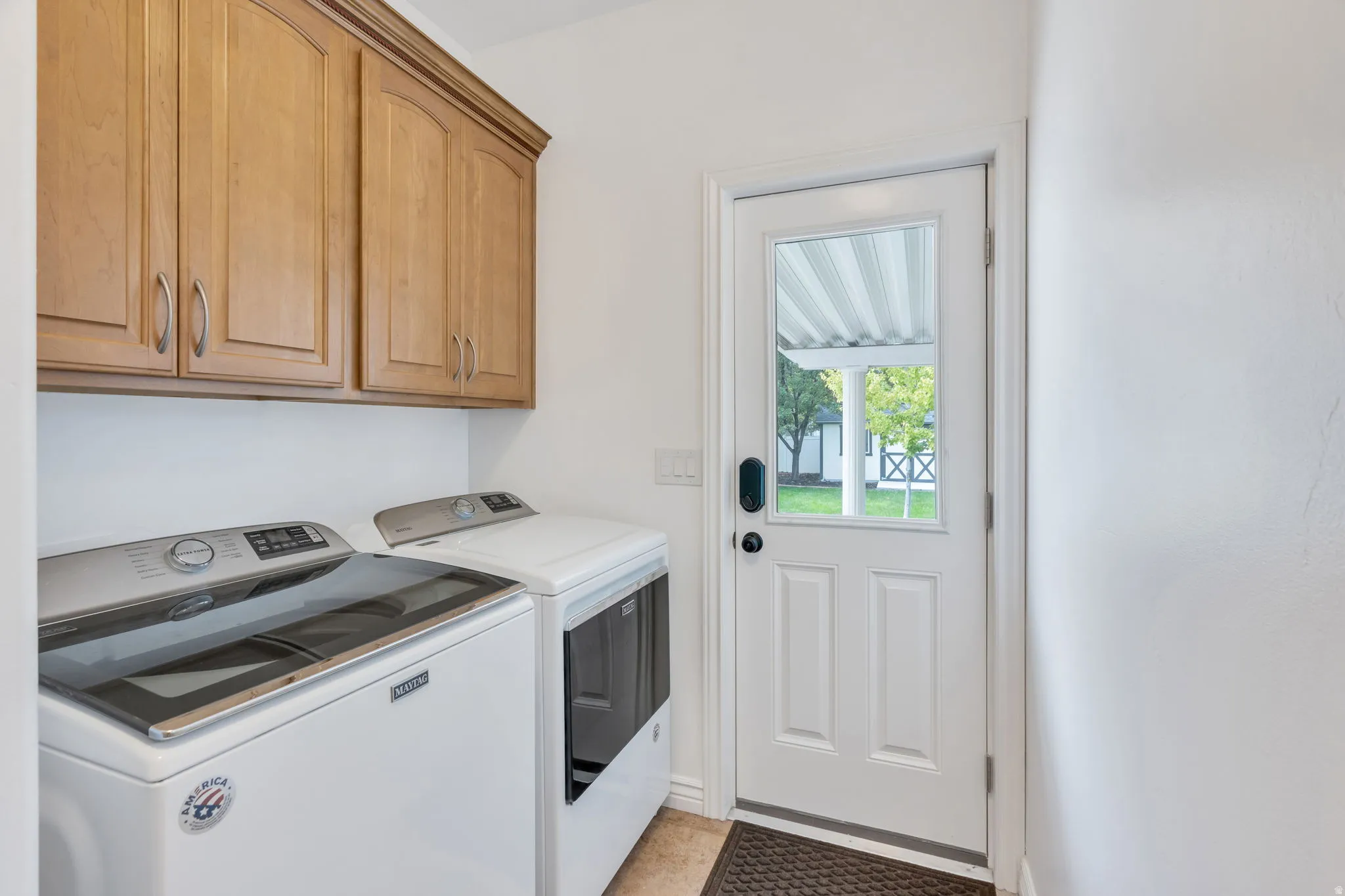 Wood-finish upper cabinetry, white painted walls, and a white exterior door with glass paneling
