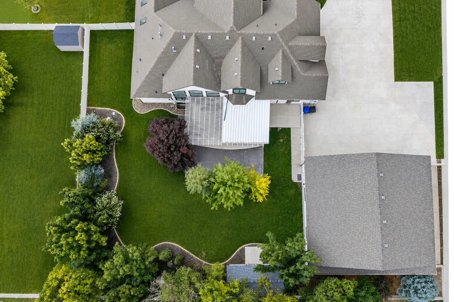 Expansive green lawn with mature landscaping, a multi-gabled roofline, and a detached storage shed