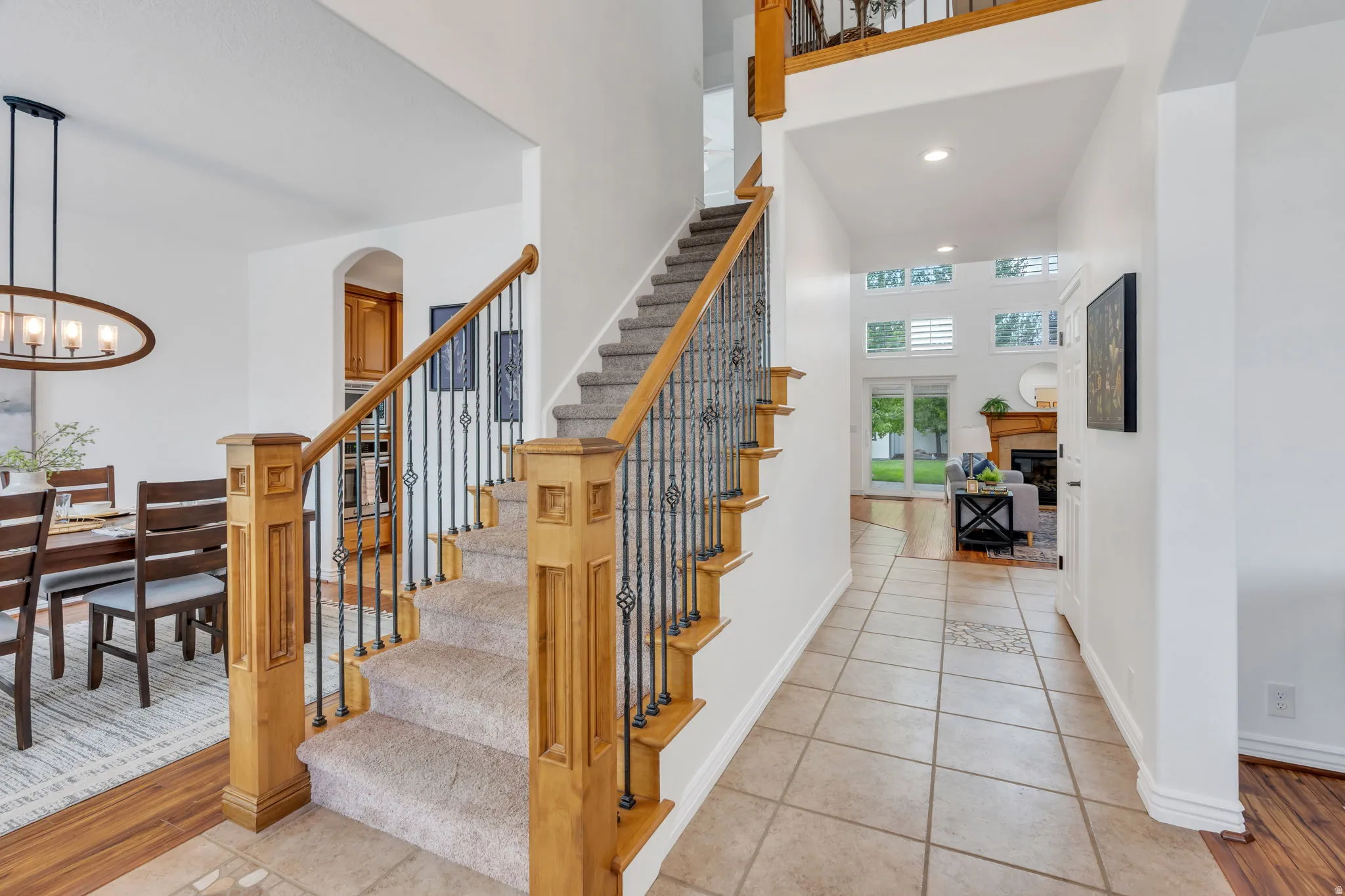 Two-story foyer with tile flooring, wood-finish staircase with wrought iron balusters, and recessed lighting