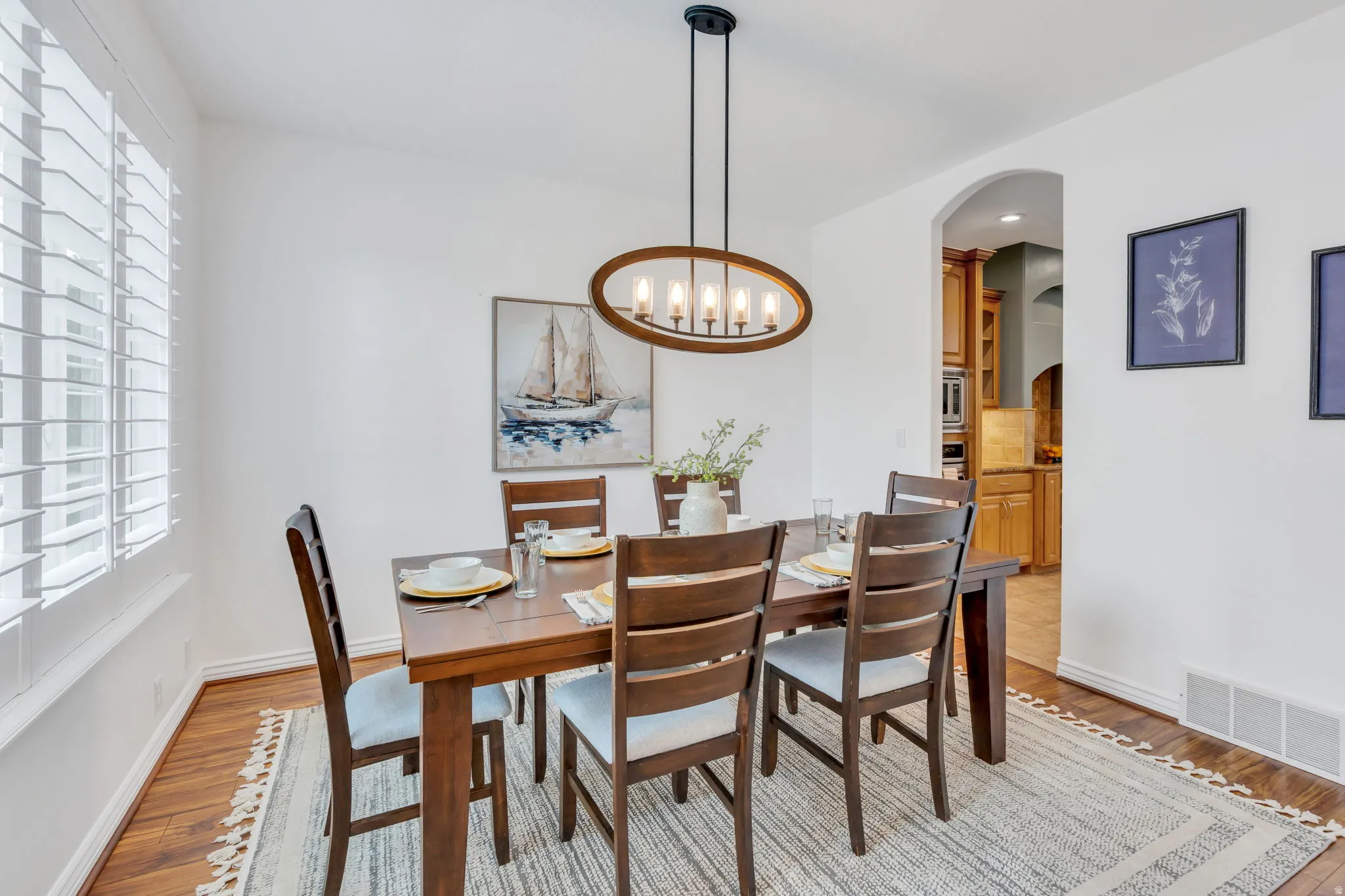 Recessed arched entryway, wood-finish flooring, plantation shutters, and a modern oval chandelier